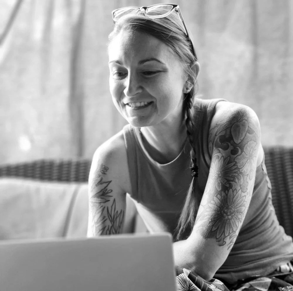 Woman with glasses perched on her head smiling while looking at a laptop