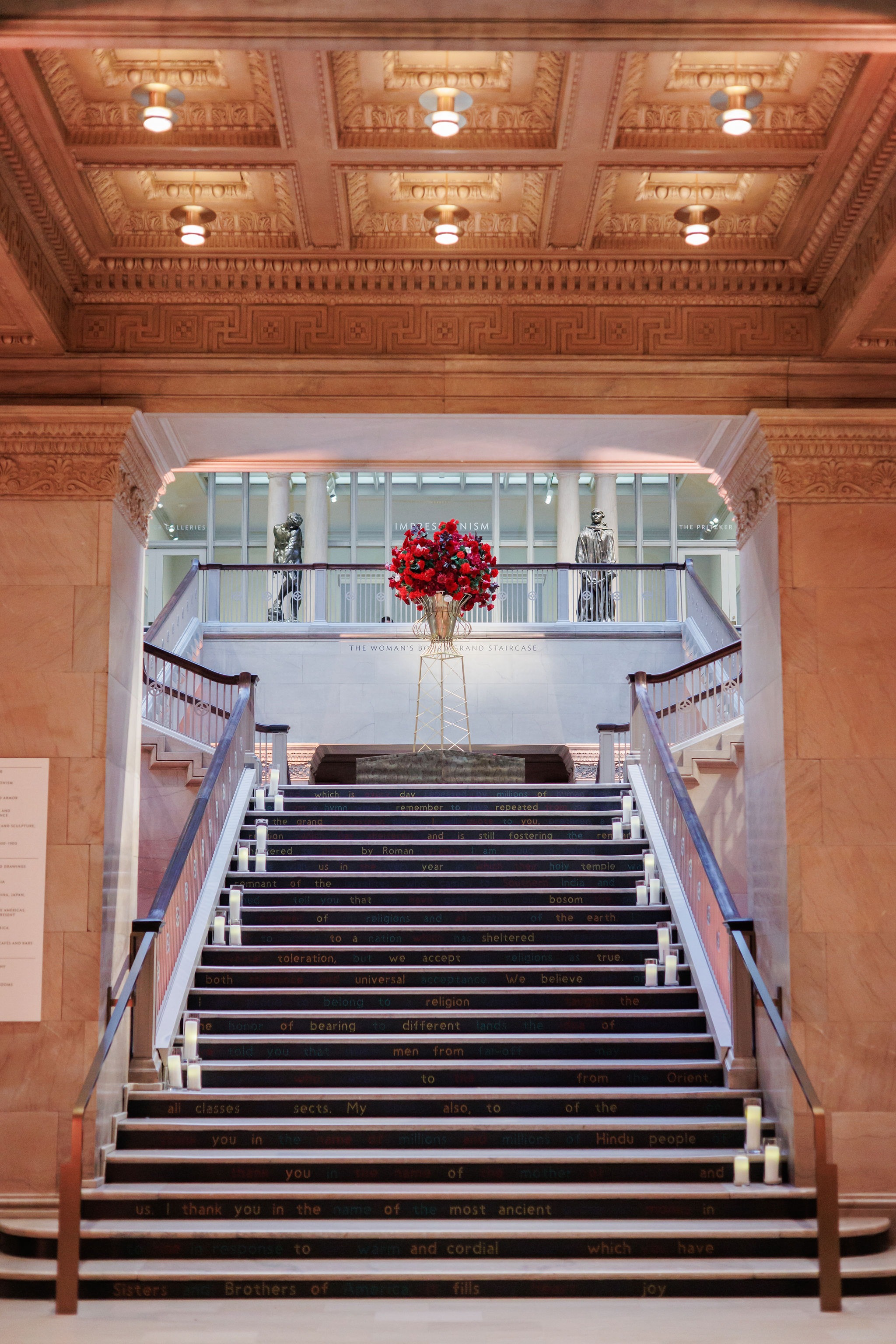 Candlelit grand staircase of the Art Institute of Chicago crowned by a red floral arrangement, seen from the entrance hall