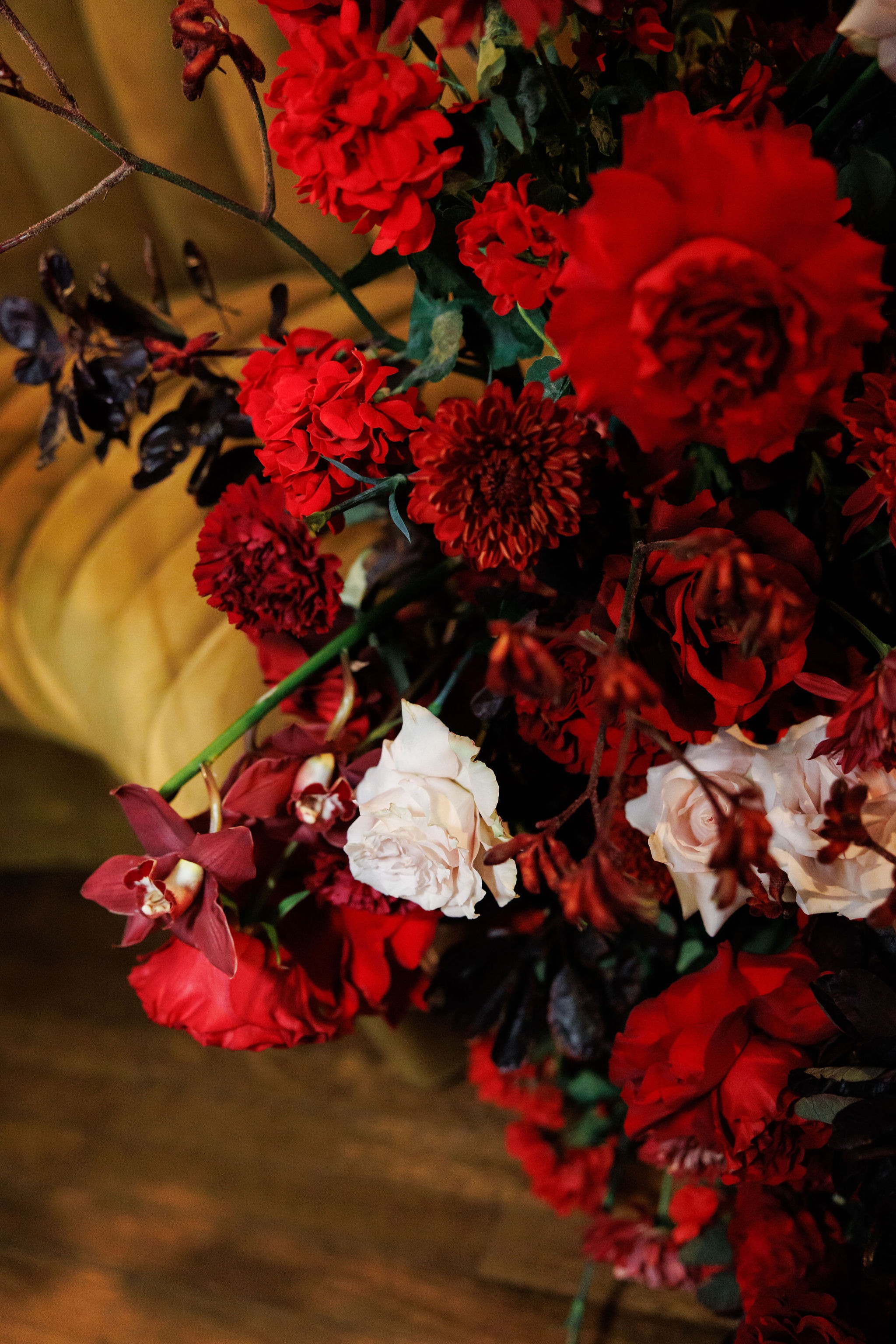 Close-up of crimson roses, burgundy orchids, dahlias, and blush blooms in a reception arrangement