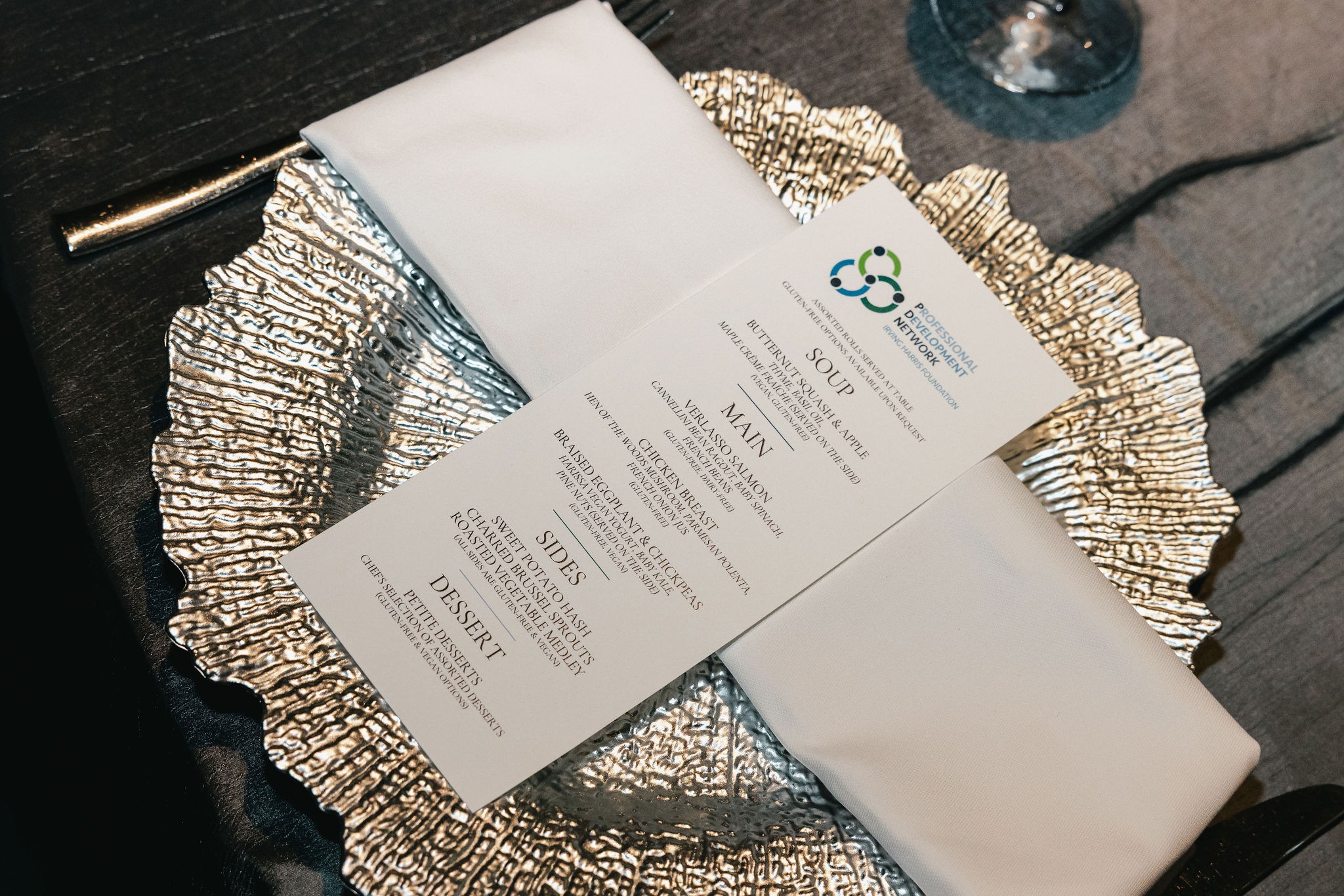Printed dinner menu on a textured silver charger at a conference place setting