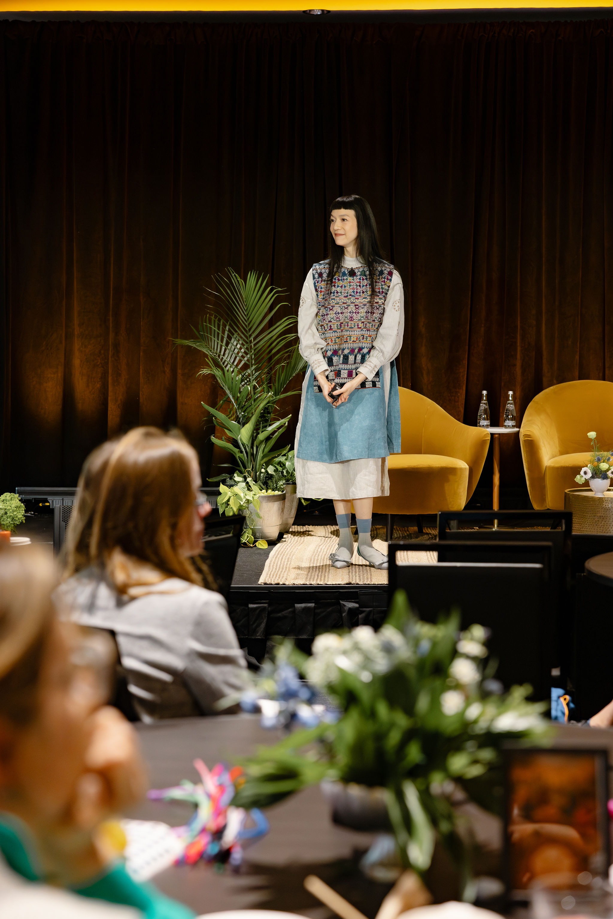 Speaker standing on a plant-lined stage before the conference audience