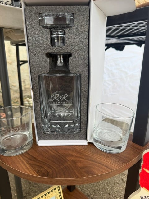 A glass whiskey decanter and two rocks glasses engraved with the R&R Laserforge logo, in a gift box