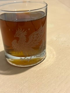 A whiskey glass engraved with a phoenix, filled with bourbon