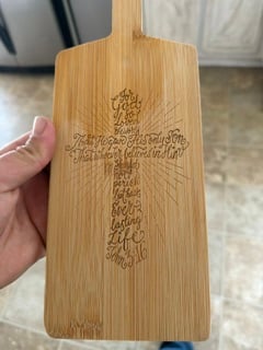 A bamboo paddle board engraved with a cross made of scripture text