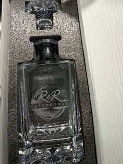 A glass whiskey decanter engraved with the R&R Laserforge logo, in its gift box