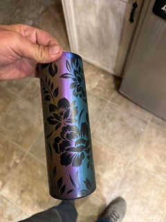 An iridescent purple and teal tumbler engraved with large flowers