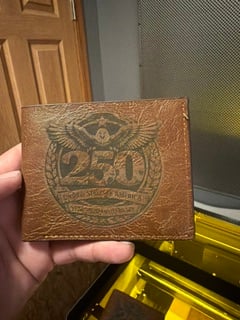 A brown leather bifold wallet engraved with a 250th anniversary eagle emblem