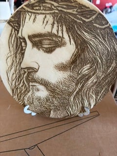 A round wooden plaque engraved with a portrait of Jesus wearing a crown of thorns