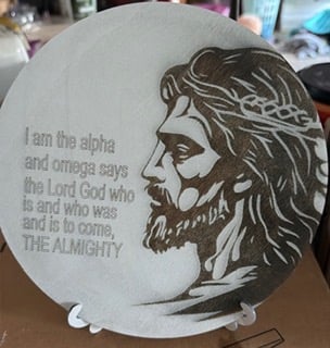 A round plaque engraved with a portrait of Jesus beside the words I am the alpha and omega