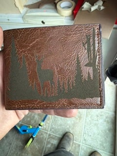 A brown leather wallet engraved with a deer standing among pine trees