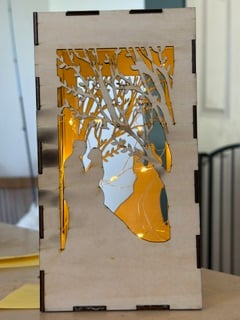 A laser-cut wooden lantern with a forest scene, glowing amber from inside